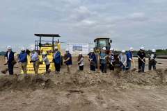 a row of men and women in hardhats turn earth with shovels in hand, all in front of large construction equipment, as part of the ground breaking ceremony for Rye Ranch Elementary School in Parrish Florida