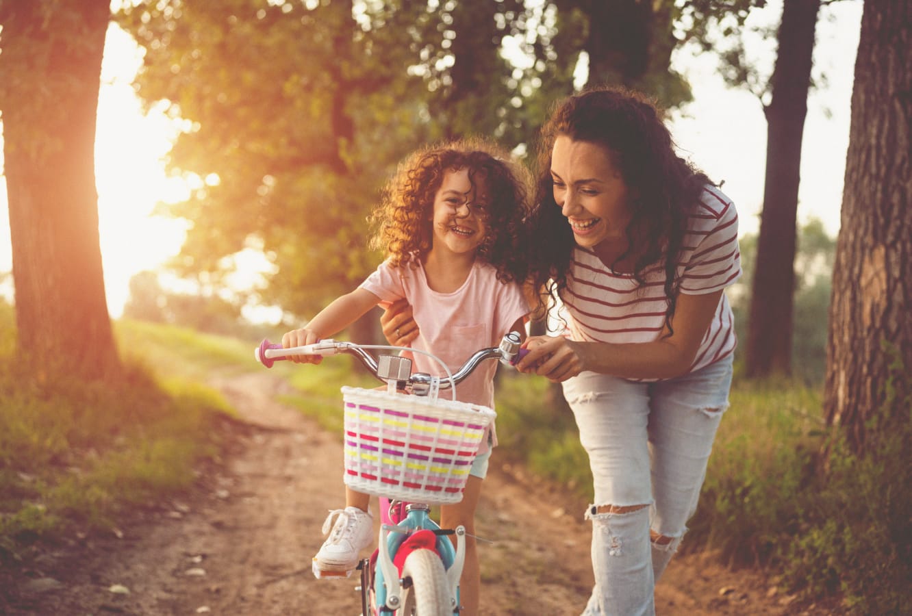 A mother teaching her daughter to ride a bike on a trail at Rye Ranch