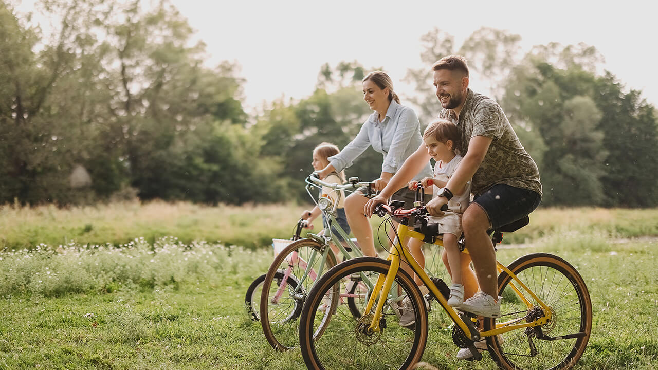 a man and woman ride bicycles with two children through a grassy meadow on a sunny day - one of many activities enjoyed after relocating to Florida