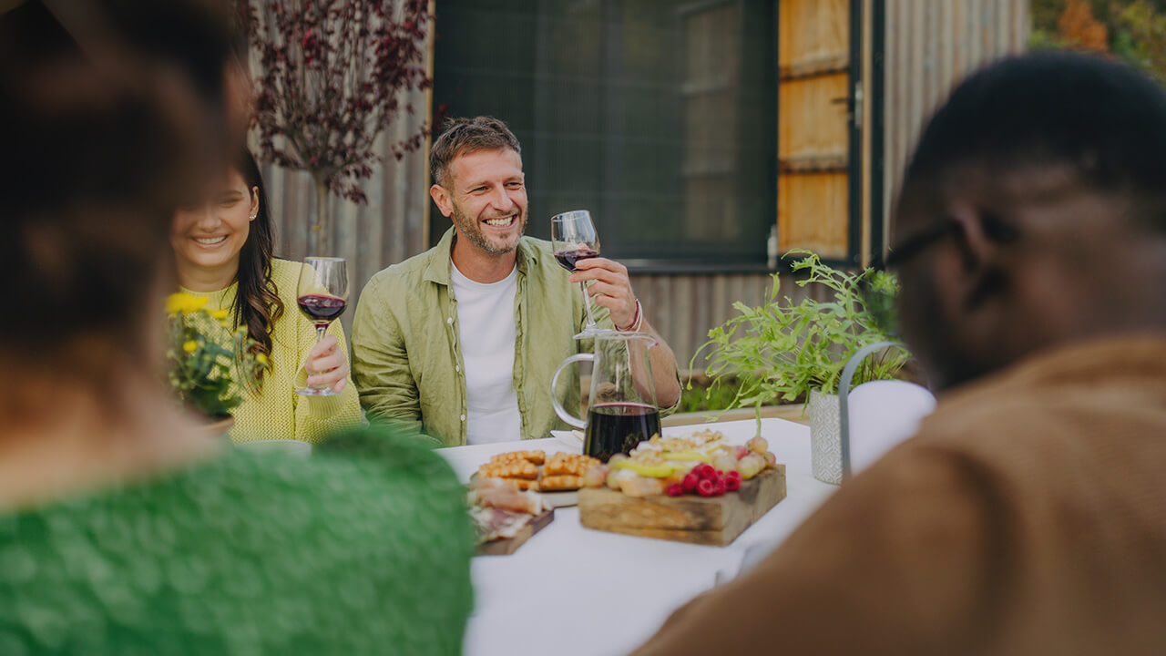 a diverse group of friends gathers around a table toasting one another with glasses of wine - Community Amenities That Elevate Everyday Living at Rye Ranch