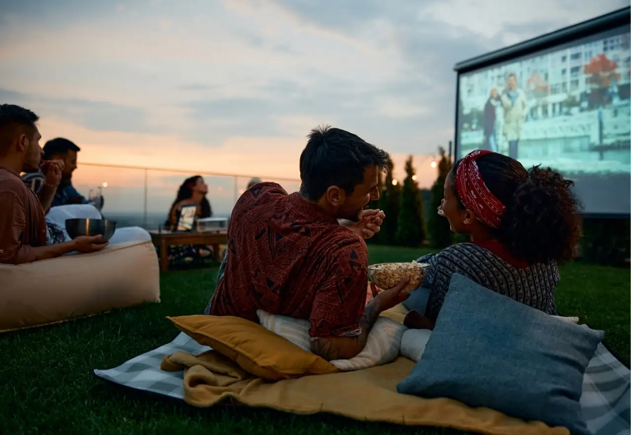 couple eating popcorn on a blanket watching an outdoor movie