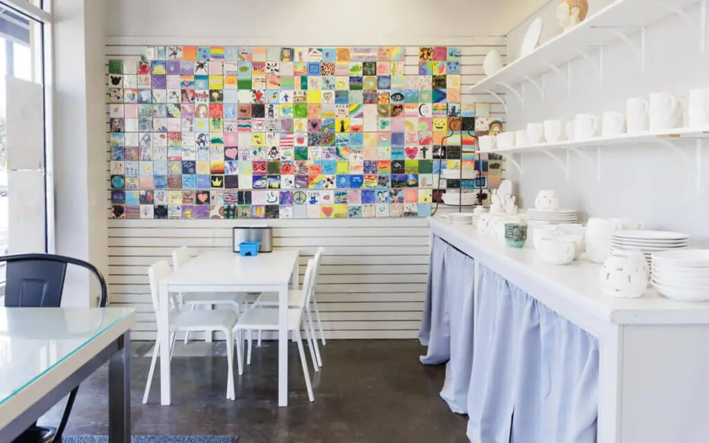 brightly lit room with white tables and chairs and a white countertop on the right including ceramic pottery ready for painting, plus colorful array of painted tiles on the far wall at Arts a Blaze - a hidden gem near Parrish Florida