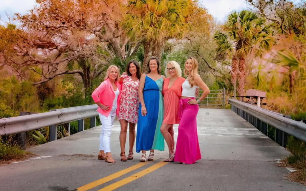 colorful scene with soft-focus palm trees in the background and five women standing on a country road, all wearing garments from Teal Turtle Boutique, a hidden gem in Parrish Florida